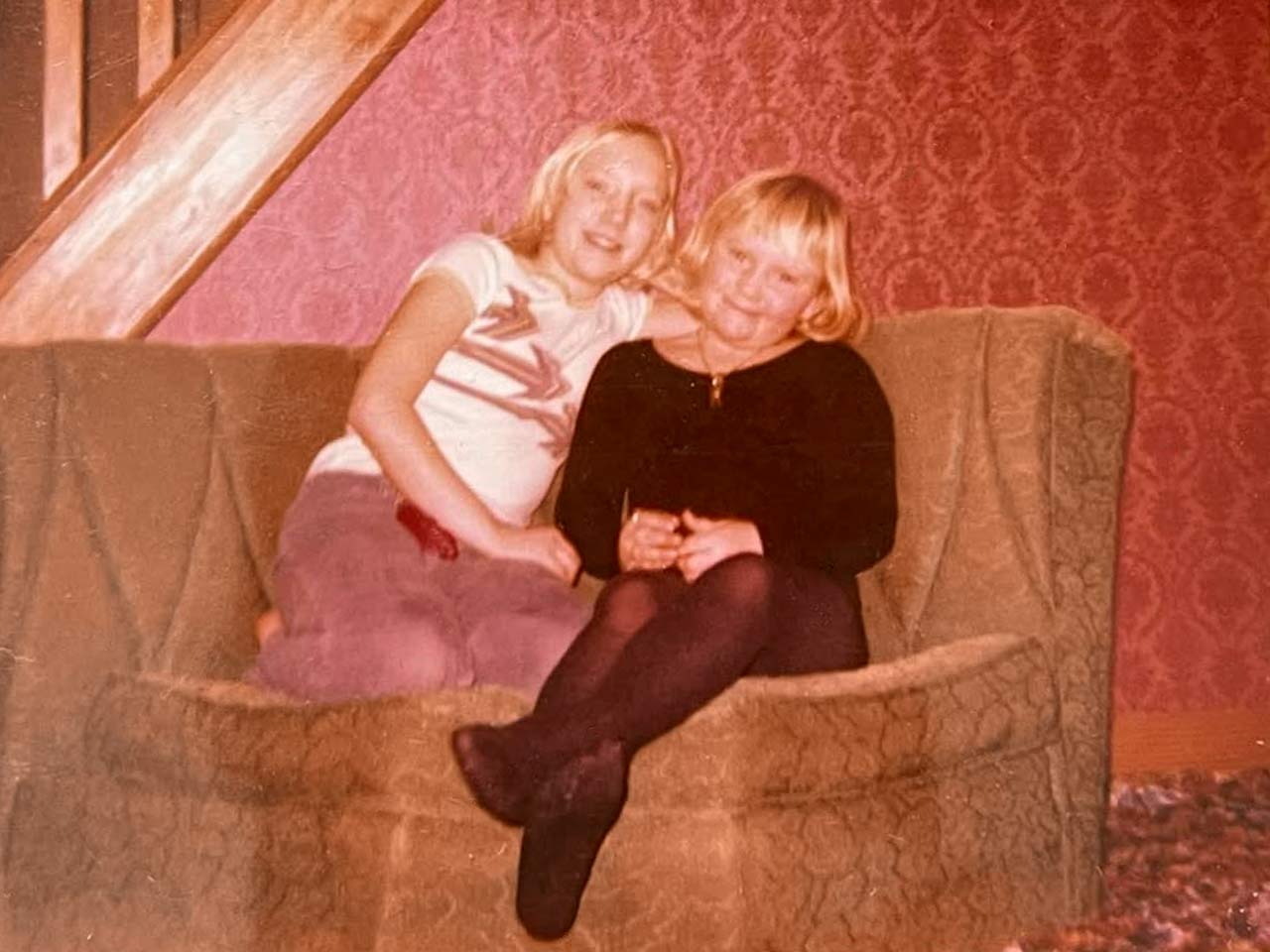 Laura and her younger sister sitting on a sofa in a warm embrace both facing the camera.